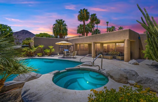 pool at dusk featuring an in ground hot tub, a patio area, and a mountain view