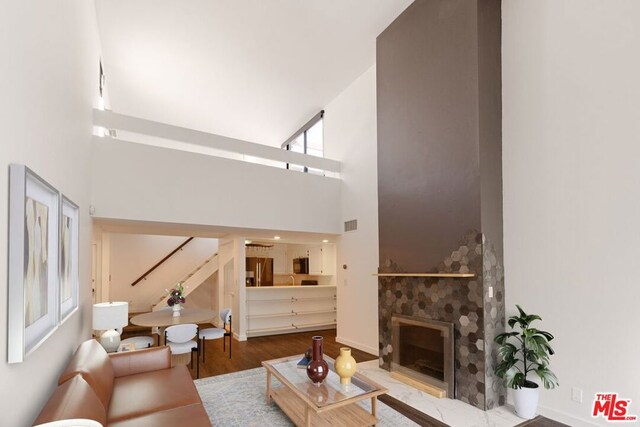 living room featuring a tiled fireplace, a towering ceiling, and wood-type flooring