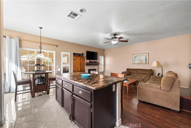 kitchen with a kitchen island, a fireplace, hanging light fixtures, ceiling fan, and dark brown cabinets