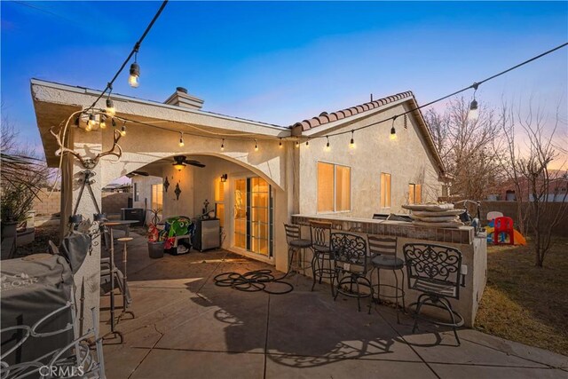 back house at dusk featuring ceiling fan, a bar, and a patio area