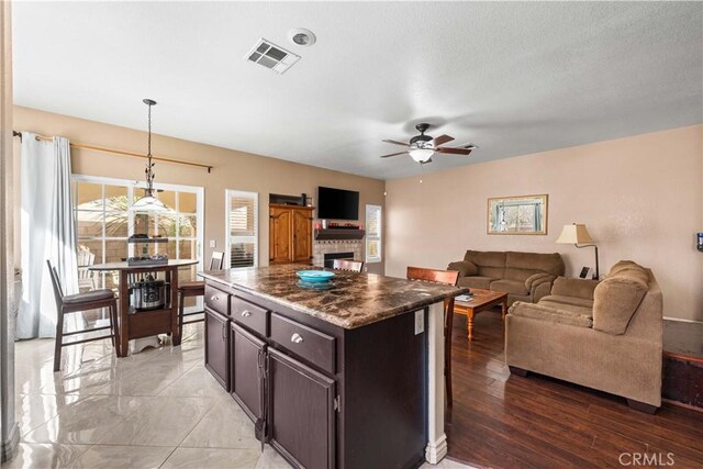 kitchen with dark brown cabinetry, a kitchen island, decorative light fixtures, a fireplace, and ceiling fan