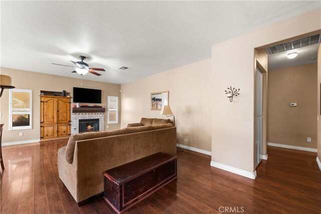 living room with ceiling fan, dark wood-type flooring, plenty of natural light, and a tiled fireplace