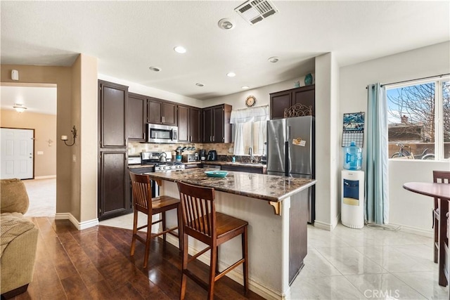 kitchen with appliances with stainless steel finishes, dark brown cabinets, a kitchen island, a breakfast bar, and sink