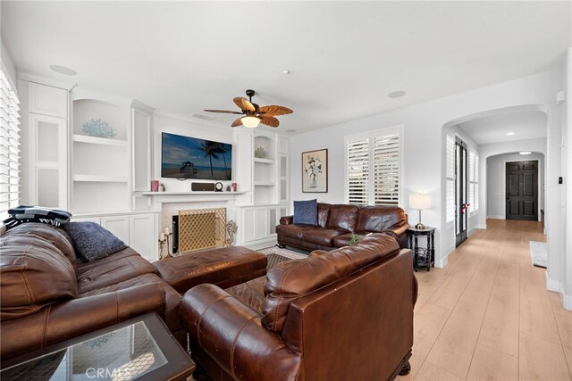 living room featuring ceiling fan, built in shelves, and light hardwood / wood-style floors