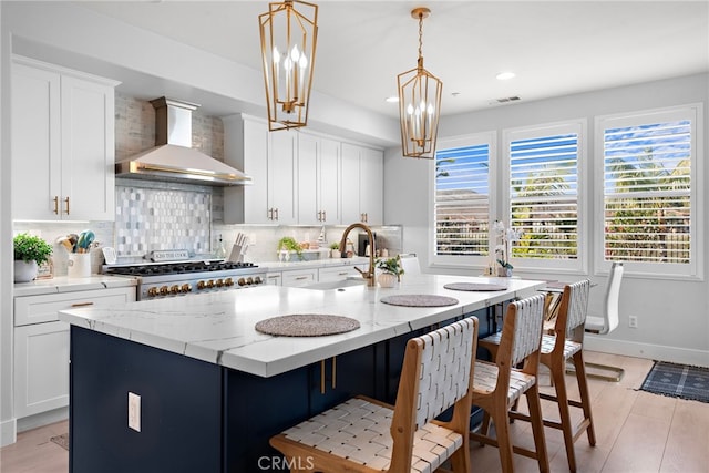 kitchen featuring decorative backsplash, wall chimney range hood, a kitchen island with sink, and pendant lighting