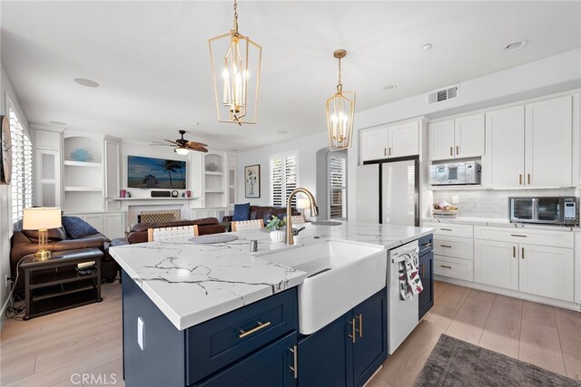 kitchen featuring sink, white appliances, hanging light fixtures, a kitchen island with sink, and blue cabinetry