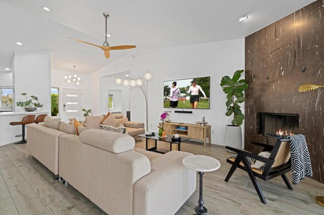 living room featuring a fireplace, lofted ceiling, ceiling fan with notable chandelier, and light hardwood / wood-style flooring