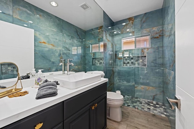 bathroom with toilet, a tile shower, hardwood / wood-style floors, and vanity