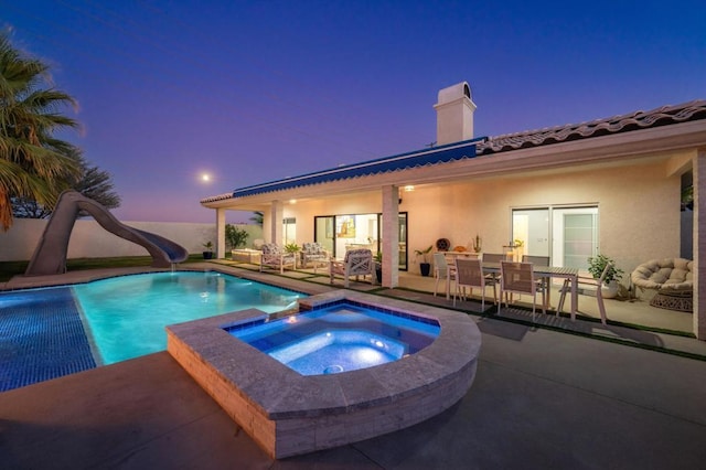 pool at dusk featuring an outdoor living space, a water slide, a patio, and an in ground hot tub