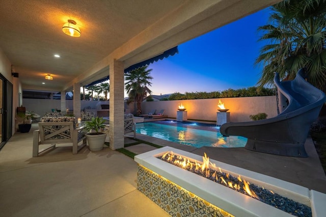 pool at dusk featuring a patio, an outdoor fire pit, and a water slide