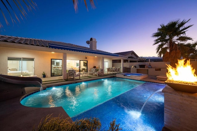 pool at dusk featuring an in ground hot tub, a patio area, an outdoor fire pit, and a water slide