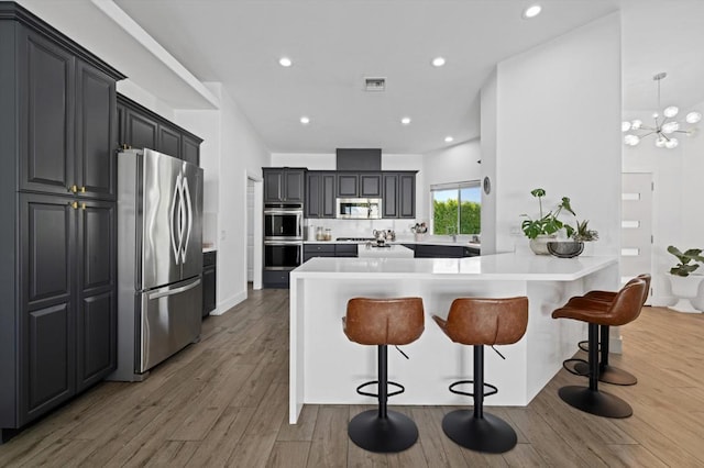 kitchen with dark hardwood / wood-style flooring, stainless steel appliances, an inviting chandelier, a kitchen breakfast bar, and kitchen peninsula