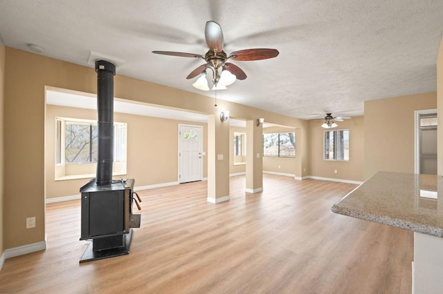 unfurnished living room featuring ceiling fan, a textured ceiling, a wood stove, and light hardwood / wood-style floors