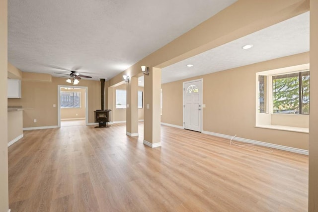 unfurnished living room with ceiling fan, light hardwood / wood-style floors, and a wood stove