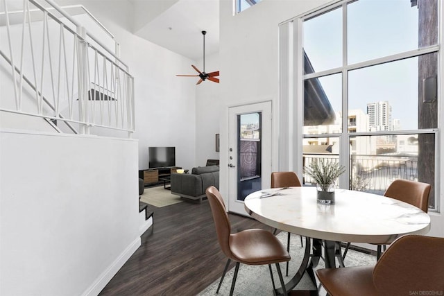 dining room featuring ceiling fan, dark wood-type flooring, and a towering ceiling