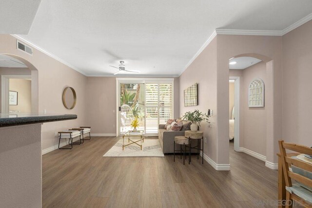 living area featuring ceiling fan, crown molding, and wood-type flooring