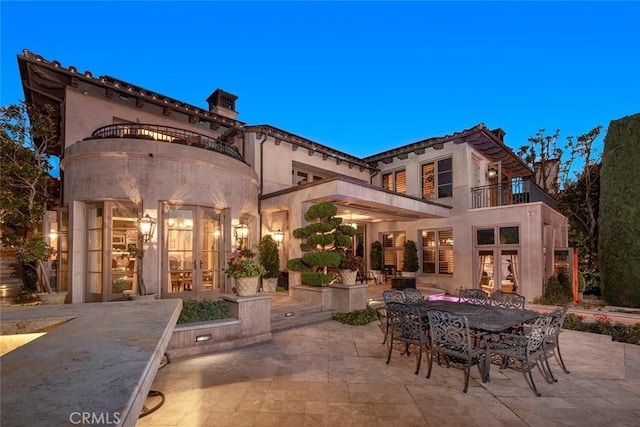 back house at dusk featuring a balcony, french doors, and a patio