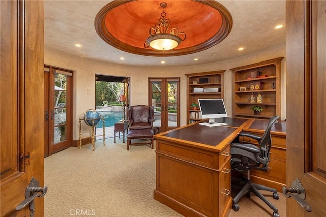 office space with light colored carpet, built in shelves, a raised ceiling, and french doors