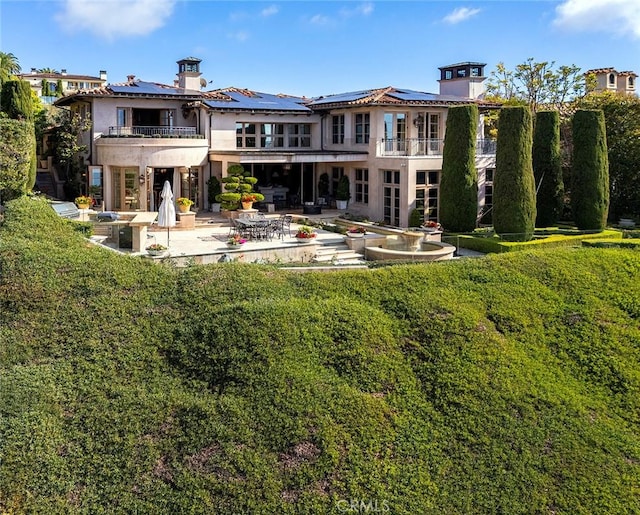 rear view of house featuring a lawn, solar panels, a balcony, and a patio