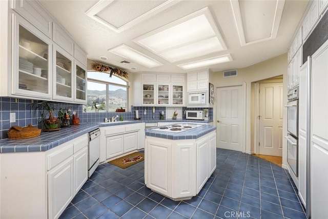 kitchen with tile countertops, a kitchen island, sink, white appliances, and white cabinetry