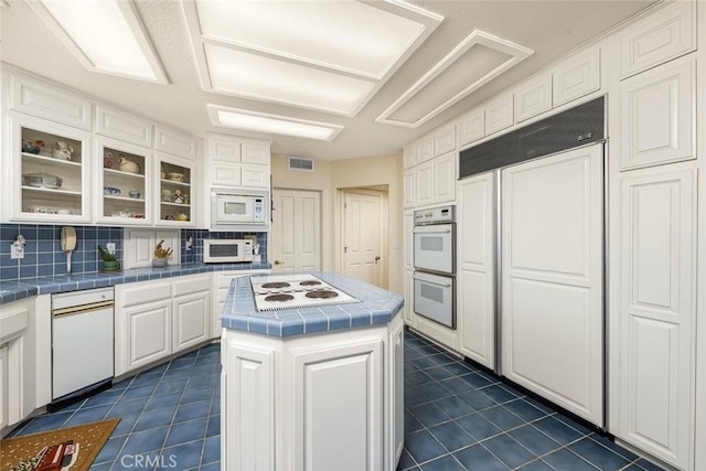 kitchen with tasteful backsplash, tile countertops, a kitchen island, built in appliances, and white cabinetry