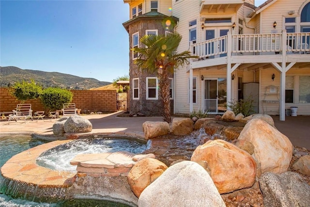 rear view of house with a balcony, a fenced in pool, a patio, a mountain view, and pool water feature