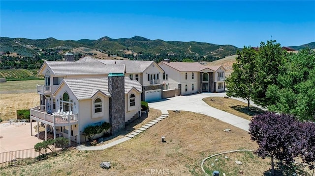 back of property with a balcony, a mountain view, a yard, and a garage