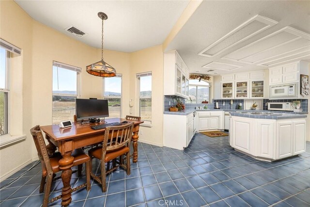 kitchen with white cabinets, white microwave, plenty of natural light, and pendant lighting