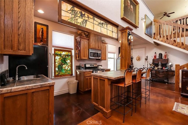 kitchen with ceiling fan, stainless steel appliances, a breakfast bar area, a kitchen island, and sink