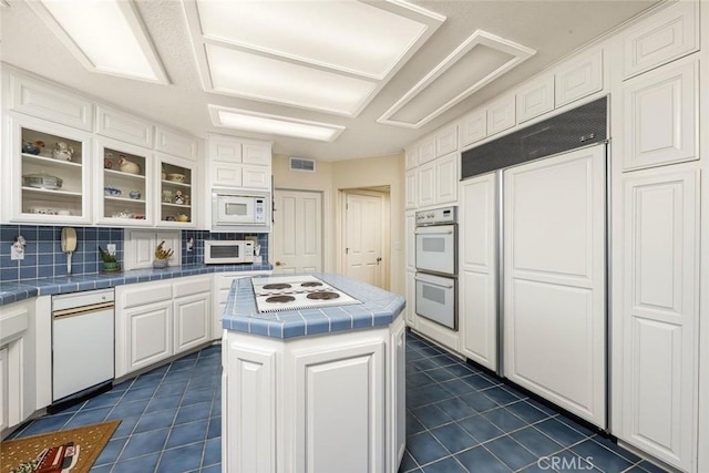 kitchen with tile countertops, built in appliances, dark tile patterned floors, and white cabinets