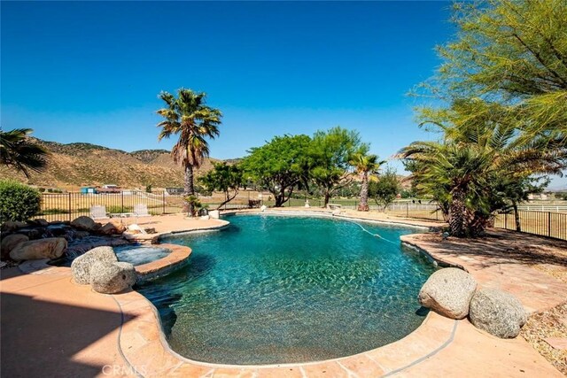 view of pool with a pool with connected hot tub, a patio area, fence, and a mountain view