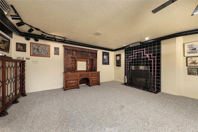 interior space featuring a ceiling fan, carpet, a textured ceiling, and a tiled fireplace