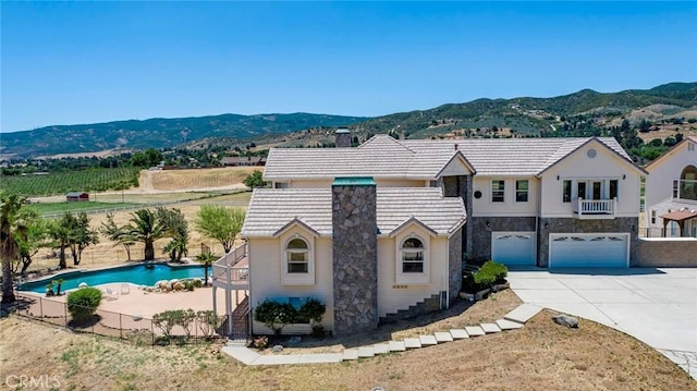 view of front of home with a garage, concrete driveway, a chimney, fence, and a mountain view