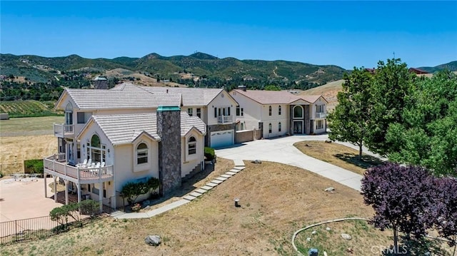 view of front facade featuring a mountain view, a balcony, a garage, fence, and concrete driveway