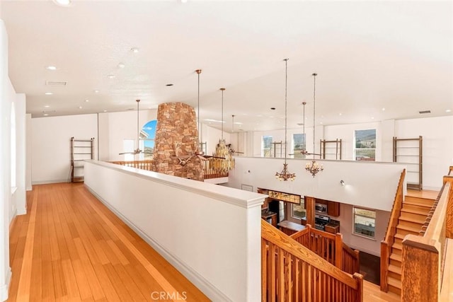 corridor featuring light wood-style floors, recessed lighting, visible vents, and an upstairs landing