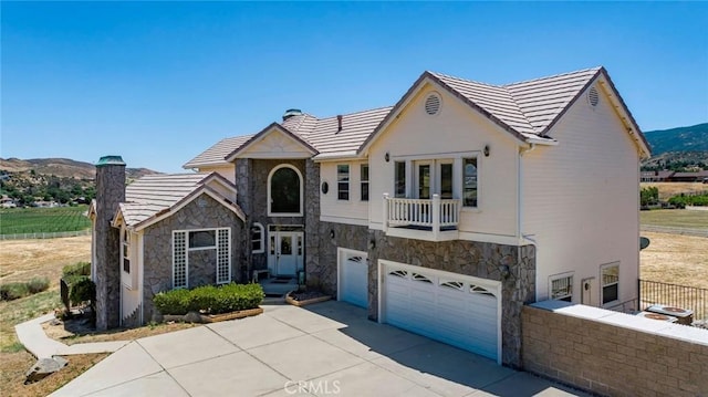 tudor house featuring stone siding, a chimney, concrete driveway, and a balcony