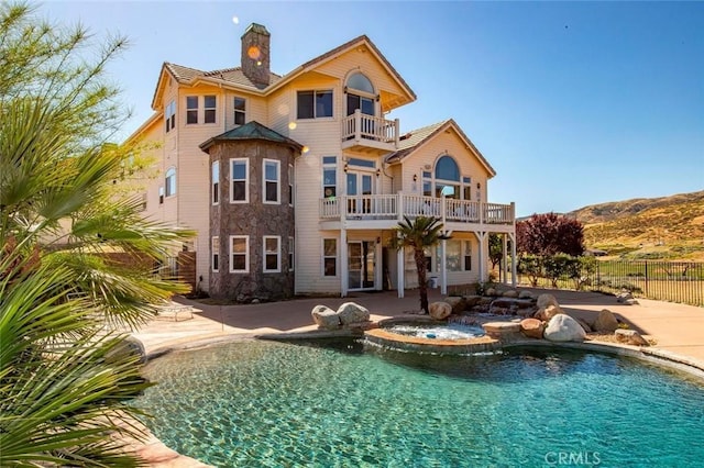 rear view of house with a chimney, a patio area, a balcony, and an in ground hot tub