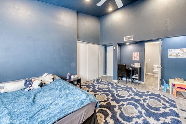 bedroom featuring connected bathroom, ceiling fan, a towering ceiling, and light hardwood / wood-style flooring