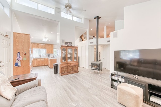 living room with ceiling fan, a high ceiling, a wood stove, and light hardwood / wood-style flooring