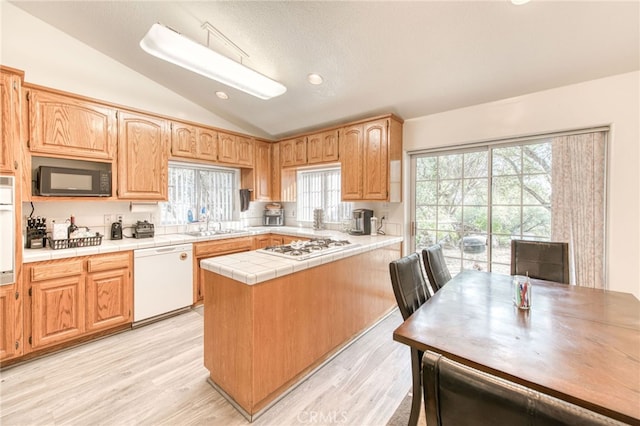 kitchen featuring white appliances, a wealth of natural light, tile counters, lofted ceiling, and light hardwood / wood-style flooring