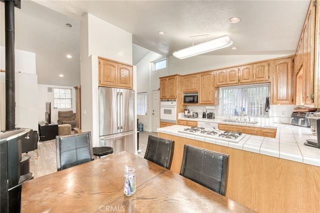 kitchen with lofted ceiling, tile countertops, sink, white appliances, and a wood stove