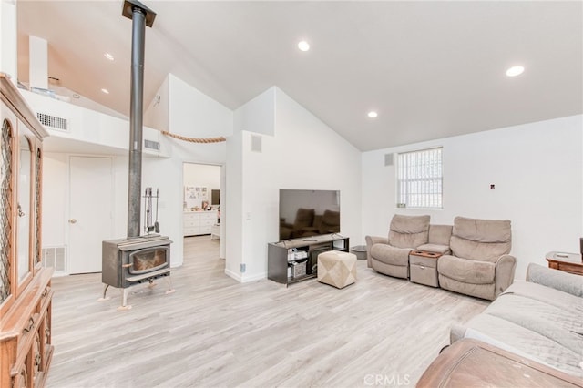 living room featuring a wood stove, light hardwood / wood-style flooring, and high vaulted ceiling