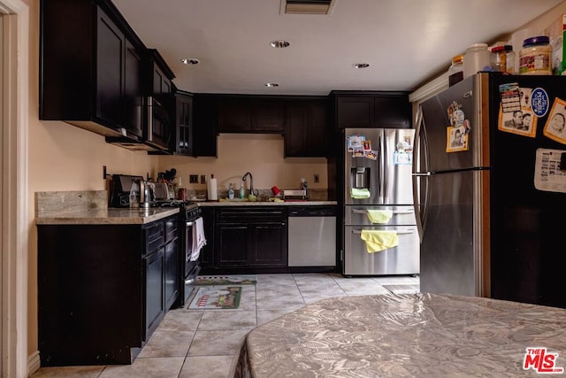 kitchen featuring light tile patterned flooring, stainless steel appliances, light stone counters, and sink