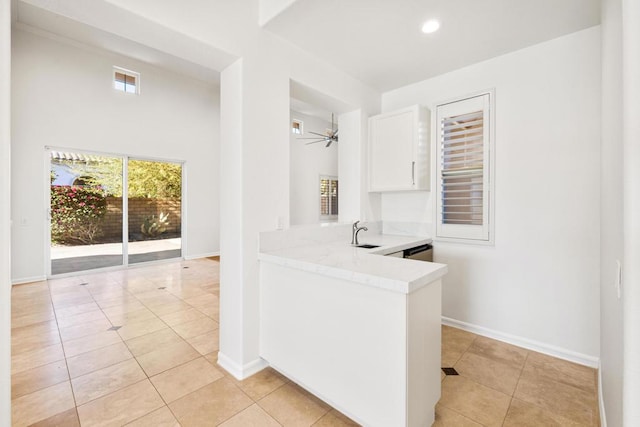 interior space featuring light tile patterned floors, white cabinetry, kitchen peninsula, ceiling fan, and sink