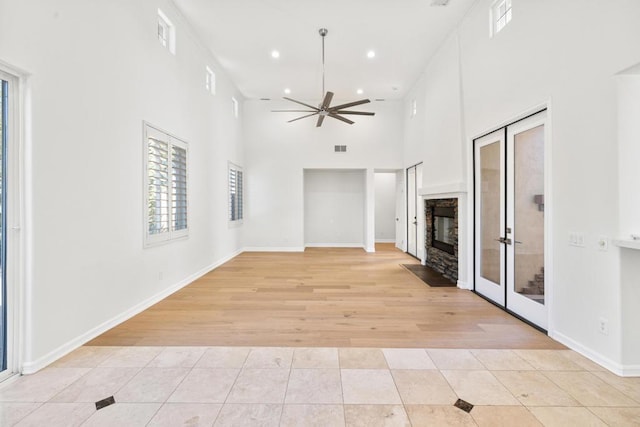 unfurnished living room with ceiling fan, light tile patterned floors, a towering ceiling, and french doors