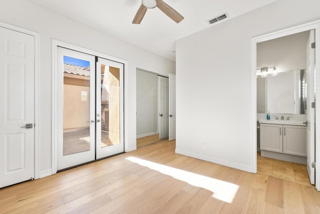 unfurnished bedroom featuring ensuite bathroom, two closets, light hardwood / wood-style floors, ceiling fan, and access to outside