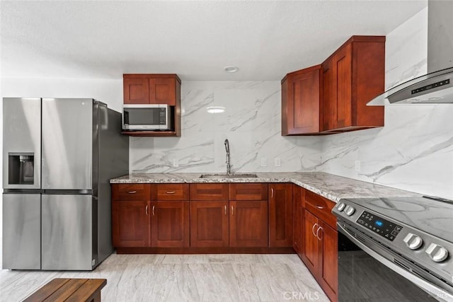 kitchen with light stone counters, a sink, decorative backsplash, appliances with stainless steel finishes, and wall chimney exhaust hood