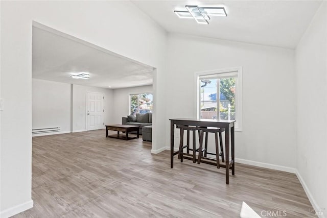 interior space featuring baseboard heating, wood finished floors, baseboards, and vaulted ceiling