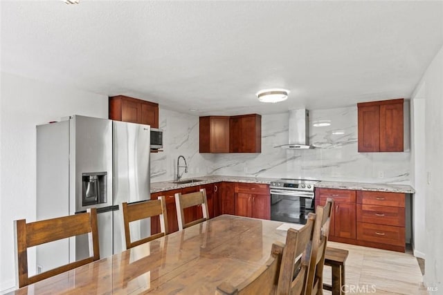 kitchen featuring backsplash, wall chimney range hood, light stone counters, appliances with stainless steel finishes, and a sink