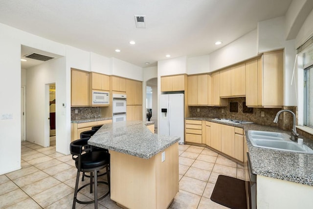 kitchen with backsplash, a center island, white appliances, light brown cabinetry, and sink